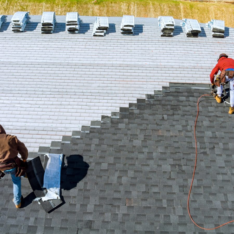Worker hands installing bitumen roof shingles with air hammer and nail